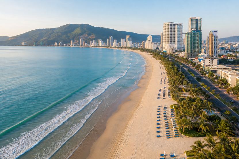 Aerial view of My Khe beach in Da Nang on a clear morning, the coastline curving north past the beach road towers toward the Son Tra peninsula