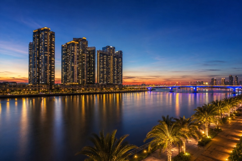 High rise apartment towers on the Han River in Da Nang lit up at dusk, with the riverside promenade in the foreground