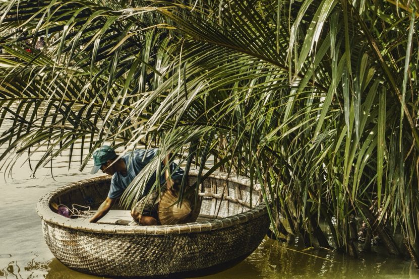 A round woven bamboo basket boat on the water under coconut palms in Cam Thanh, near Hoi An